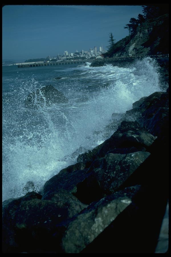 005049 Waves Breaking On Rocks With City, Jetty A4 Photo Print