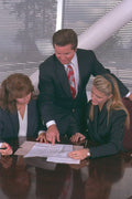 719006 A Man And Two Women Looking Over Contracts At Table A4 Photo Print